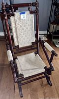 Wooden rocking chair with fabric back and seat, shown in full view on hardwood floor.