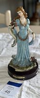 Full view of the porcelain figurine showing a woman in a blue dress holding a bouquet of roses.