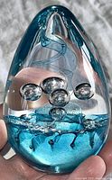 Front and side view of the egg-shaped glass paperweight showing blue internal ribbon swirl and air bubbles.