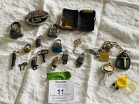 All items laid out on fabric including 13 locks mostly with keys, keychains, belt buckle, and dice case