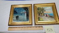 Two hand painted art tiles, one with boat in water under arch, the other with group walking on seaside path, both in gold frames placed on white surface with ruler for size.
