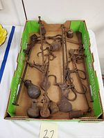 Top-down view of multiple antique cast iron hanging hook scales and assorted cast iron weights in a cardboard box.