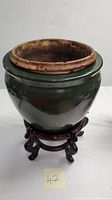 Large dark green glazed ceramic planter pot supported by a wooden stand with a removable rustic brown ceramic inner liner visible on top