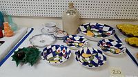 Photo showing various ceramic items arranged on a table including a stoneware jug, blue and white striped fruit bowls with painted fruit, artisan plates, a soup mug with lid, and a holly ivy dish.