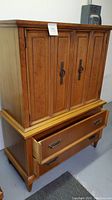 Front angle view showing upper cabinet with four paneled doors, metal ring handles, and open lower drawer with metal pulls, highlighting finish and style