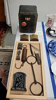 Photo of the lot arranged on a tray and table including Frontier Safe coin bank, brass bookends, pencil sharpeners, straight razor, and hanging scale.