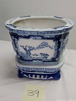 Blue and white ceramic planter with Asian landscape designs shown from front angle.