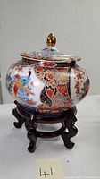 Full view of the lidded tureen on its lacquered wood stand, showing shape and lid with golden knob