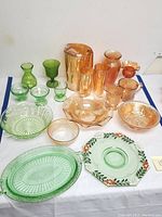 Full lot display showing two sections: green carnival glassware including plates, bowls, and small vases; and amber/uranium glass pitchers and drinkware with ruffled glass bowls.
