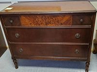 Front view of vintage wooden dresser showing three drawers and decorative inlay on top middle drawer