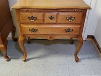 Front view of vintage wooden writing desk showing the drawer handles, wood finish, legs, and scalloped apron with carved shell detail.
