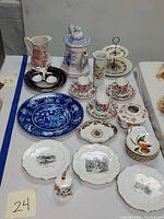 Full view of assortment of vintage porcelain dishes, plates, cups, teapot and pitcher with floral and scenic designs on a table