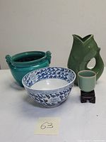 Photo showing entire lot with fish-shaped green GurglePot vase, blue and white planter bowl, turquoise planter, and small pale green cup with wooden stand on white surface.