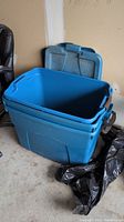 Open blue plastic tote with lid in the background, showing lid locking features and handles.