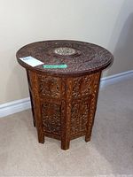 Full view of the round carved wood table showing the detailed vertical panels and the round top.