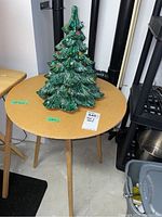 14 inch ceramic Christmas tree with colored lights on top of small round wooden table with three legs