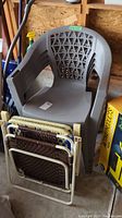 Four grey plastic backyard chairs stacked, lattice backs, plus two folding chairs with woven rope seats and backs stacked in front; one folding chair incomplete
