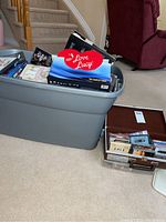 Blue large plastic tote filled with DVDs and media, with 'I Love Lucy' DVD box set visible on top, next to a smaller clear plastic container with multiple media items inside.