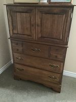 Full view of wooden highboy chest showing two paneled doors on top, three drawers below with vintage brass handles.