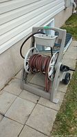 View of entire garden hose mounted on beige hose reel with crank handle and wheels outdoors on concrete tiles.