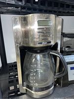 Front view of Oster 12-cup coffee maker with glass carafe, showing stainless steel finish and digital buttons