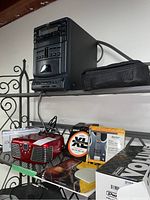 Side view of black JVC multi-disc CD player, red Magnasonic player, cassette player, guitar strings and Dunlop volume pedal box on shelf