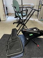 Black metal keyboard stand, microphone stand, guitar stand, Dixon bench, Voyageur guitar case, denim cover in basement setting.
