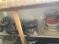Photo showing stacked metal pots and saucepans with wooden handles, glass casseroles and a clear glass vase