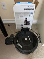 Photo of iRobot Roomba vacuum and base charger with Panasonic phone box in background showing included phone system