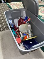 Grey plastic tote filled with assorted sewing and knitting supplies such as yarn, needles, scissors, thread, buttons, and containers.