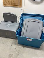 Shows two large totes, one grey Sterilite 30-gallon tote with lid, and one blue Rubbermaid tote with hinged lid. Additional lids are visible.