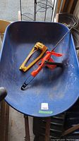 Blue metal Yardworks wheelbarrow with garden hand tools inside including hedge trimmer and pruners