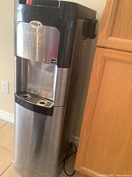 Full view of Whirlpool water cooler and heater unit, showing stainless steel and black design with spout and drip tray.