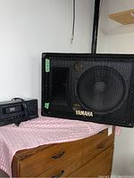 Full view of Yamaha speaker cabinet with metal grille and Optimus stereo cassette deck on a furniture surface covered with red and white checkered cloth.