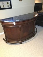 Front view of semi-circular bar showing wood base, black marble top, and foot rail
