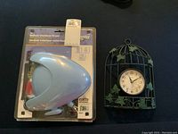 Photo of the indoor-outdoor dryer in its original plastic packaging alongside the decorative wall clock designed like a birdcage with ivy leaves.