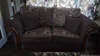 Front view of two-seat fabric sofa with floral cushions and wooden trim
