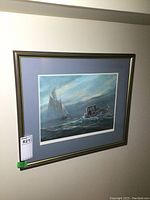 Framed signed print hanging on wall showing maritime scene with sailboat and motorboat.