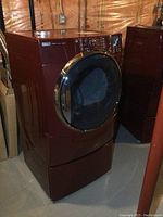 Burgundy red Kenmore Elite front load dryer on pedestal, angled front view