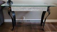 Front view of hall table showing black cast iron curved legs and detailed claw feet, stone decorative panel and clear beveled glass top