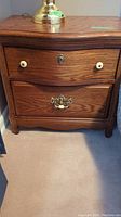 Front view of wooden nightstand showing two drawers, curved face top drawer, and decorative outside edges.