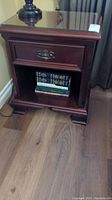 Front view of solid mahogany nightstand with one drawer, lower open shelf containing books, and glass top visible.