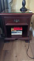 Front view of solid mahogany nightstand with single drawer, open lower shelf holding books and clear glass top.