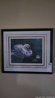 Framed artwork showing a swan on water with a light colored matting and black frame, photo taken to show the full item