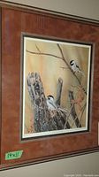Framed print showing two chickadees on a tree stump with branch and autumn leaves, matted in brown, with frame edges visible.