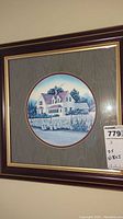 Framed print showing a rural farmhouse with milk bottles in the foreground, in blue and white tones, surrounded by an oval mat and dark wood frame with gold trim.