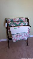 Front view of wood quilt rack holding folded floral quilt, showing its full height and width.