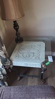 Full view of side table with stone square decorative base and cast iron legs, lamp on top for scale only