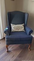 Front view of the Vogel wing back chair showing dark blue patterned upholstery, wooden cabriole legs, and decorative pillow on seat.
