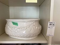Front view of the white ceramic bowl showing ornate raised patterns of fruit and bows around the body.